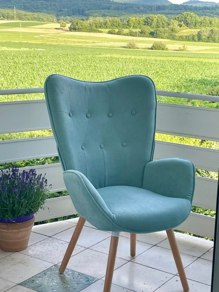 Bequemer, hellblauer Stuhl  auf einem Balkon mit Blick ins Grüne zur schwäbischen Alb.